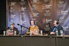 Thumbnail for Three men wearing headphones sit at a table with microphones in front of a backdrop promoting The Shrimp Tank podcast.