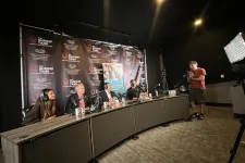 Thumbnail for Four hosts wearing headphones talk behind a curved desk with Shrimp Tank banners and a cameraman filming them.