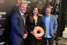 Thumbnail for Three professionals posing at The Shrimp Tank event with branded backdrop and shrimp-shaped award