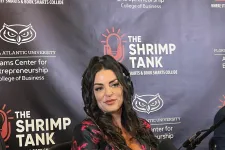Thumbnail for Woman sitting at desk with bowl of shrimp, microphone, and branded backdrop of The Shrimp Tank entrepreneurship event.