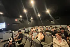 Thumbnail for Group of young adults seated in a dark room with cinema-style chairs and bright filming lights