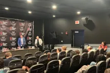 Thumbnail for Panel discussion in conference room with seated audience and speakers in front of branded backdrop under bright lights