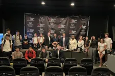 Thumbnail for Group photo of diverse people standing and sitting in front of The Shrimp Tank branded backdrop in an event setting.