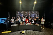 Thumbnail for Group photo of attendees at a media event, featuring a branded backdrop and diverse individuals holding merchandise.