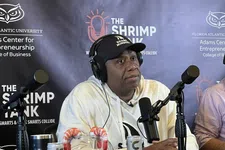 Thumbnail for Man wearing headphones and a Shark Mindset cap speaking into a microphone at The Shrimp Tank podcast setup
