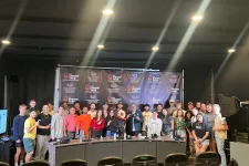 Thumbnail for Large group of people posing in front of The Shrimp Tank backdrop with studio lighting and microphones.
