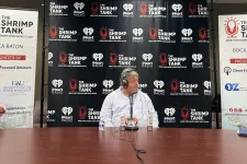 Thumbnail for a couple of men sitting at a table with microphones and a sign