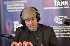 Thumbnail for Man wearing headphones and a cap speaking into a microphone at a podcast setup with shrimp-themed decorations and energy drinks.