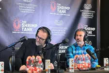Thumbnail for Two men with headphones recording The Shrimp Tank podcast with branded backdrop and shrimp bowls on the desk