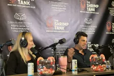 Thumbnail for Two podcasters with headphones talk into microphones in front of a backdrop for The Shrimp Tank podcast at Florida Atlantic University.