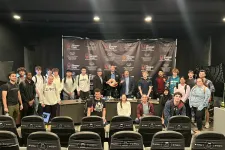 Thumbnail for Large diverse group posing in front of The Shrimp Tank branded backdrop in an event space with empty chairs in foreground