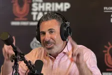 Thumbnail for Podcast host wearing headphones speaking into a microphone with energy drinks and water on the table in front.