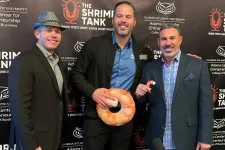 Thumbnail for Three men posing at The Shrimp Tank event with branded backdrop, shrimp-shaped item, and recording equipment.