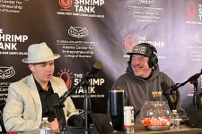 Thumbnail for Two men recording a podcast at The Shrimp Tank with microphones and branded backdrop from Florida Atlantic University