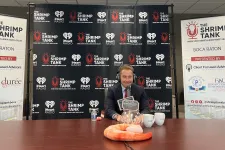 Thumbnail for a person sitting at a table with a trophy and a sign behind him