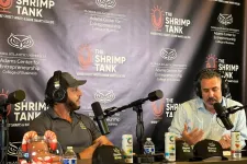 Thumbnail for Two men wearing headphones speaking into microphones at The Shrimp Tank podcast backdrop with drinks and hats on the table