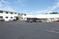 Thumbnail for Large white commercial building with restaurant equipment sign and parked vehicles under blue sky.