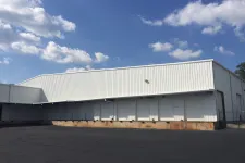 Thumbnail for White industrial warehouse with multiple loading dock doors under a partly cloudy blue sky.