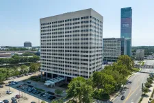 Thumbnail for Modern office building with large windows surrounded by trees and parking lots under clear blue sky