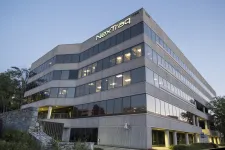 Thumbnail for Modern office building of NexTraq with illuminated logo at the top corner during early evening.