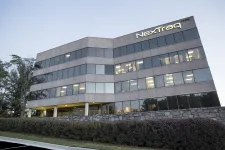 Thumbnail for Modern office building with large windows and NextTraq logo at dusk surrounded by greenery and stone wall.