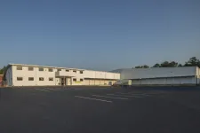 Thumbnail for Large white industrial warehouse with empty parking lot under clear blue sky in daylight.