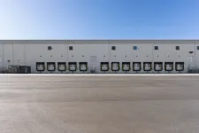 Thumbnail for Warehouse exterior with multiple loading dock doors under a clear blue sky and empty asphalt foreground