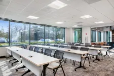 Thumbnail for Bright modern conference room with large windows, rows of tables and black chairs, and carpeted floor.