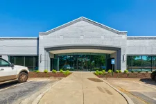Thumbnail for Modern gray brick commercial building entrance with glass doors and parking spaces under clear blue sky