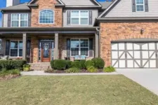 Thumbnail for Two-story suburban house with brick and siding exterior, large windows, front porch, and a double garage under blue sky.