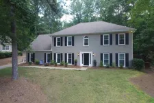 Thumbnail for Two-story gray brick house with black shutters surrounded by trees and a spacious front yard.