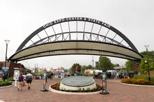Thumbnail for Entrance arch to Ohio Expo Center & State Fair with visitors and tents under cloudy sky