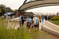 Thumbnail for Crowd walking towards amusement park entrance with ferris wheel and colorful tents in the background.