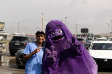 Thumbnail for Young woman standing next to a large purple mascot posing with peace signs in a parking lot.