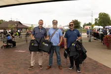 Thumbnail for Three men holding Telhio Credit Union branded bags at an outdoor event with tents and people in the background