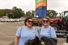 Thumbnail for Two women wearing light blue Telhio Credit Union shirts hold branded black drawstring bags outdoors.