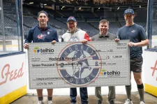 Thumbnail for Four men on an ice hockey rink holding a large Telhio Credit Union check for $7,280 made out to Hockey & Hounds.