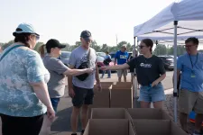 Thumbnail for Volunteers distributing items to people at an outdoor event under a white tent with cardboard boxes