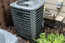 Thumbnail for AC Maintenance, Cleaning and Tune-up in Johns Creek by The Air Company of GA.  Two outdoor air conditioning units near a wooden fence and siding with green leafy plants in front.