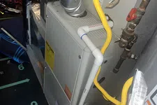 Thumbnail for AC Preventative Maintenance in Tucker, Atlanta by The Air Company of GA. Close-up of a home furnace system with metal vent pipes and yellow gas tubing connected to plumbing.