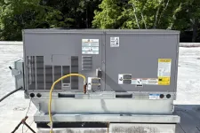 Thumbnail for Commercial rooftop HVAC unit with gray metal casing and yellow gas line on flat roof with trees in background