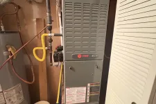 Thumbnail for Trane XR80 furnace installed in a utility room next to a water heater and cleaning tools under soft lighting.