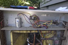 Thumbnail for Exposed internal components and wiring of an HVAC unit with compressor and capacitors visible.
