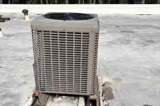 Thumbnail for Rooftop HVAC air conditioning unit with fan on top, mounted on aged concrete platform near forest trees.