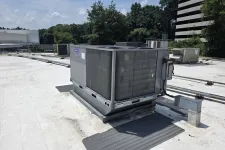 Thumbnail for Commercial rooftop HVAC unit installed on a flat white roof under a sunny sky with trees and nearby buildings.