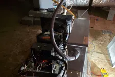 Thumbnail for Open HVAC system unit with exposed wiring and ductwork in basement under repair with testing tool nearby.