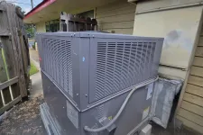 Thumbnail for Large outdoor HVAC unit installed beside a beige building under a red-trimmed roof on concrete pad