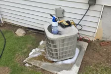 Thumbnail for Outdoor air conditioning unit on concrete pad beside house with cleaning supplies on top and green grass surrounding.