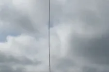 Thumbnail for Long thin antenna mounted on rooftop with multiple HVAC units under cloudy sky in daytime