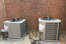 Thumbnail for Two outdoor HVAC units installed on concrete pads against a brick wall with connected piping and wiring.